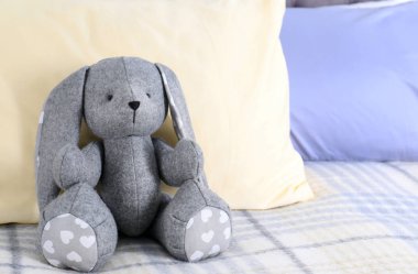 Kapalı yatağın üstüne oturan sevimli oyuncak tavşan. Metin için yer