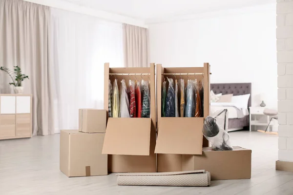Κουτιά από χαρτόνι ντουλάπα με ρούχα σε κρεμάστρες, λάμπα και χαλί στην κρεβατοκάμαρα — Φωτογραφία Αρχείου