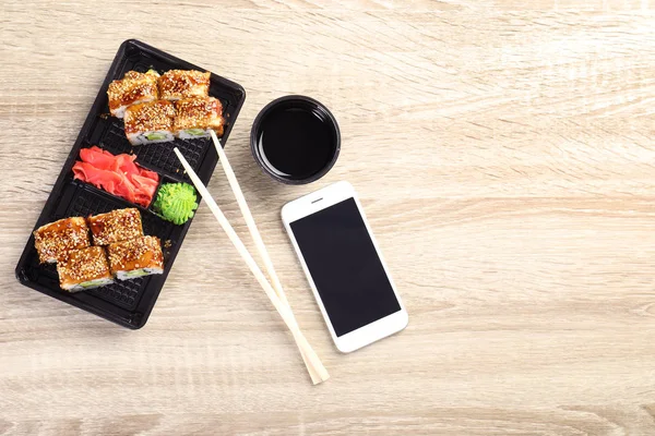 Composição de leigos planos com rolos de sushi e smartphone em mesa de madeira, espaço para texto. Entrega de alimentos — Fotografia de Stock