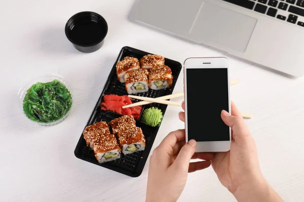 Woman with mobile phone and sushi rolls at table, space for text. Food delivery — Stock Photo, Image