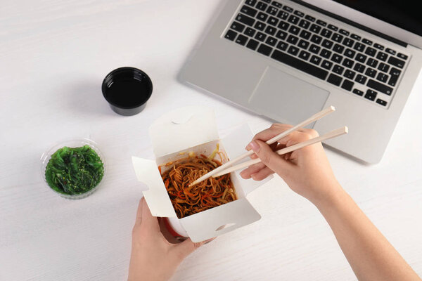 Woman eating tasty Chinese noodles at workplace, closeup. Food delivery