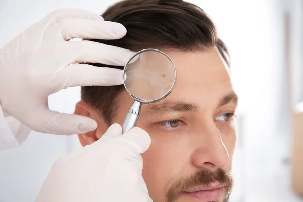Dermatologo che esamina la voglia del paziente con lente d'ingrandimento in clinica — Foto Stock