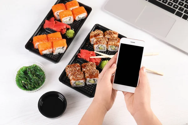 Kvinna med mobiltelefon och sushi rullar vid bordet, utrymme för text. Matleveranser — Stockfoto