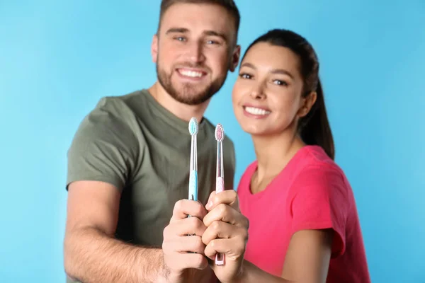 Νεαρό ζευγάρι με οδοντόβουρτσες σε έγχρωμο φόντο. Φροντίδα των δοντιών — Φωτογραφία Αρχείου