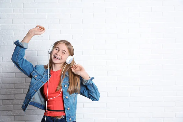 Teen dziewczyna słuchanie muzyki przez słuchawki w pobliżu mur z cegły. Miejsca na tekst — Zdjęcie stockowe