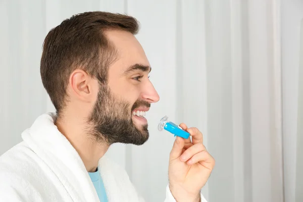 Young man using teeth whitening device on light background. Space for text — Stock Photo, Image