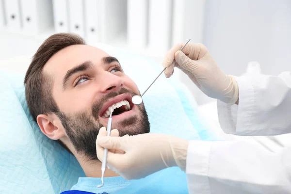 Zahnarzt untersucht Zähne des jungen Mannes mit Spiegel und Sonde im Krankenhaus — Stockfoto