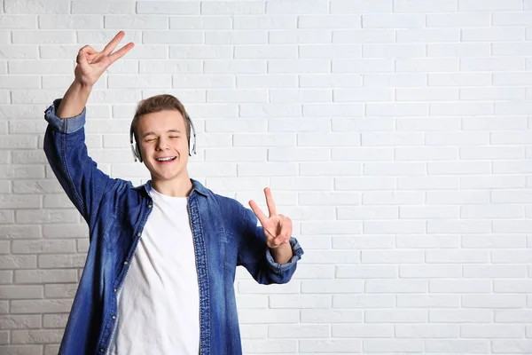 Adolescent garçon écoute de la musique avec casque près mur de briques, espace pour texte — Photo