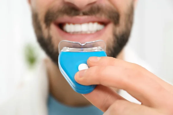 Young man using teeth whitening device on light background, closeup — Stock Photo, Image