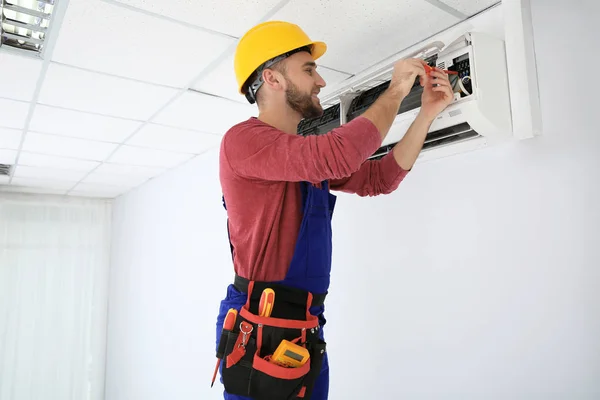 Eletricista com chave de fenda reparando ar ar condicionado dentro de casa — Fotografia de Stock