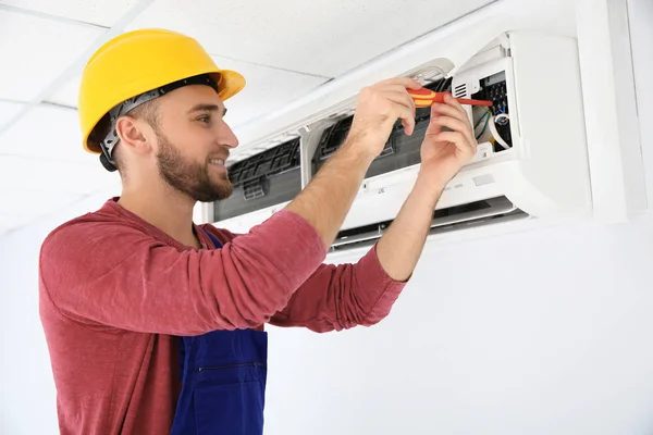 Eletricista com chave de fenda reparando ar ar condicionado dentro de casa — Fotografia de Stock
