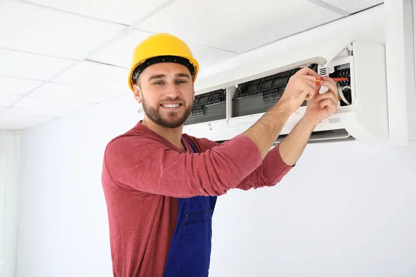 Electricista con destornillador reparando aire acondicionado en interiores —  Fotos de Stock