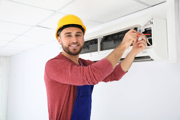 Electrician with screwdriver repairing air conditioner indoors