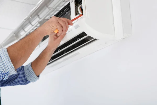 Electrician with screwdriver repairing air conditioner indoors, closeup — Stock Photo, Image