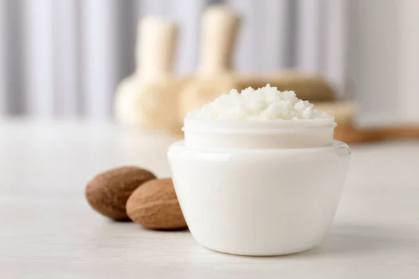 Jar of shea butter and nuts on table against blurred background. Space for text — Stock Photo, Image