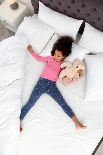 Мила дівчинка афро-американських з ведмедиком спати в ліжку, вид зверху — стокове фото