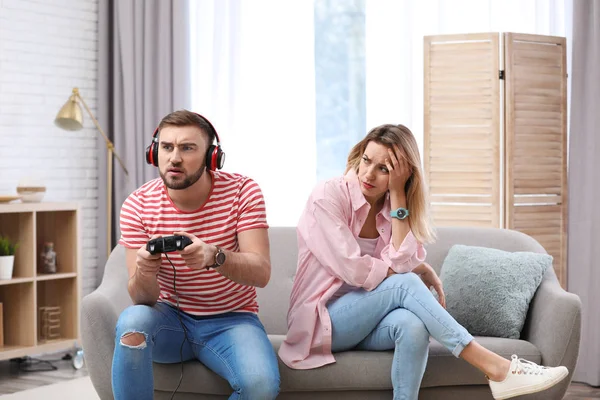 Joven jugando videojuego en casa mientras su novia se enoja con él — Foto de Stock