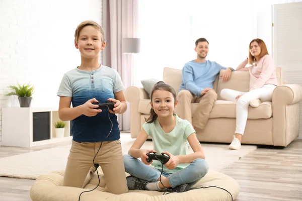 Lindos niños jugando videojuegos mientras los padres descansan en el sofá en casa — Foto de Stock