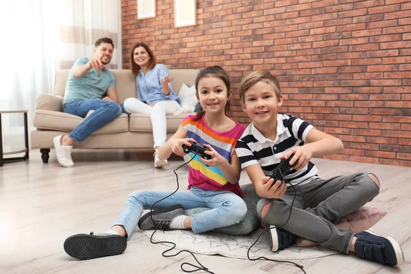 Bambini svegli che giocano ai videogiochi mentre i genitori riposano sul divano a casa — Foto Stock