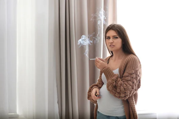 Jeune femme enceinte fumant une cigarette à la maison. Dommage pour le bébé à naître — Photo