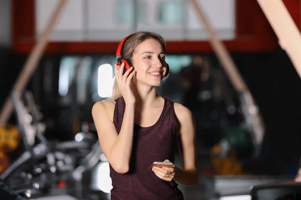 Mujer joven con auriculares escuchando música en el dispositivo móvil en el gimnasio — Foto de Stock