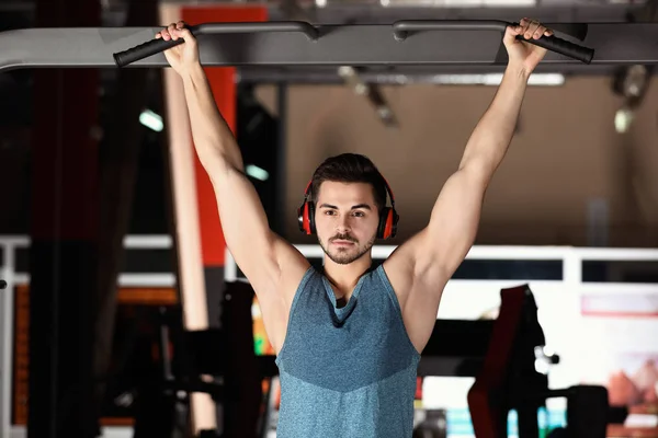 Joven con auriculares escuchando música y haciendo ejercicio en el gimnasio — Foto de Stock