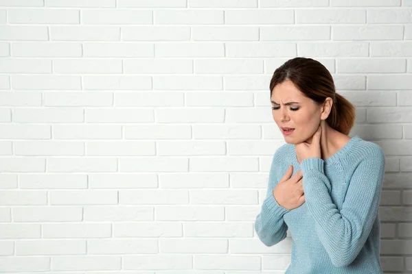 Kvinna som lider av hosta nära tegelvägg. Utrymme för text — Stockfoto