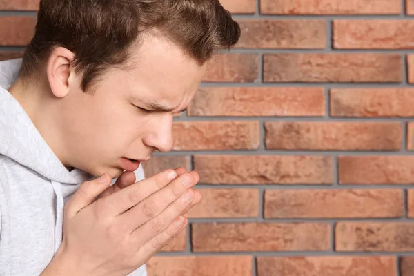 Adolescente que sufre de tos cerca de la pared de ladrillo. Espacio para texto —  Fotos de Stock