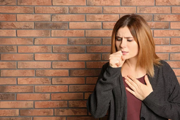 Mulher que sofre de tosse perto da parede de tijolo. Espaço para texto — Fotografia de Stock