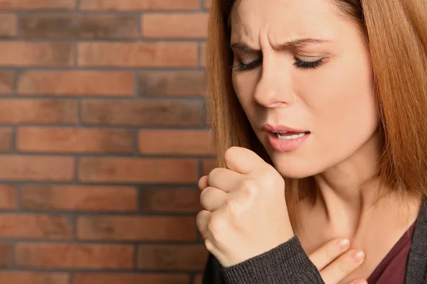 Mujer que sufre de tos cerca de la pared de ladrillo. Espacio para texto —  Fotos de Stock