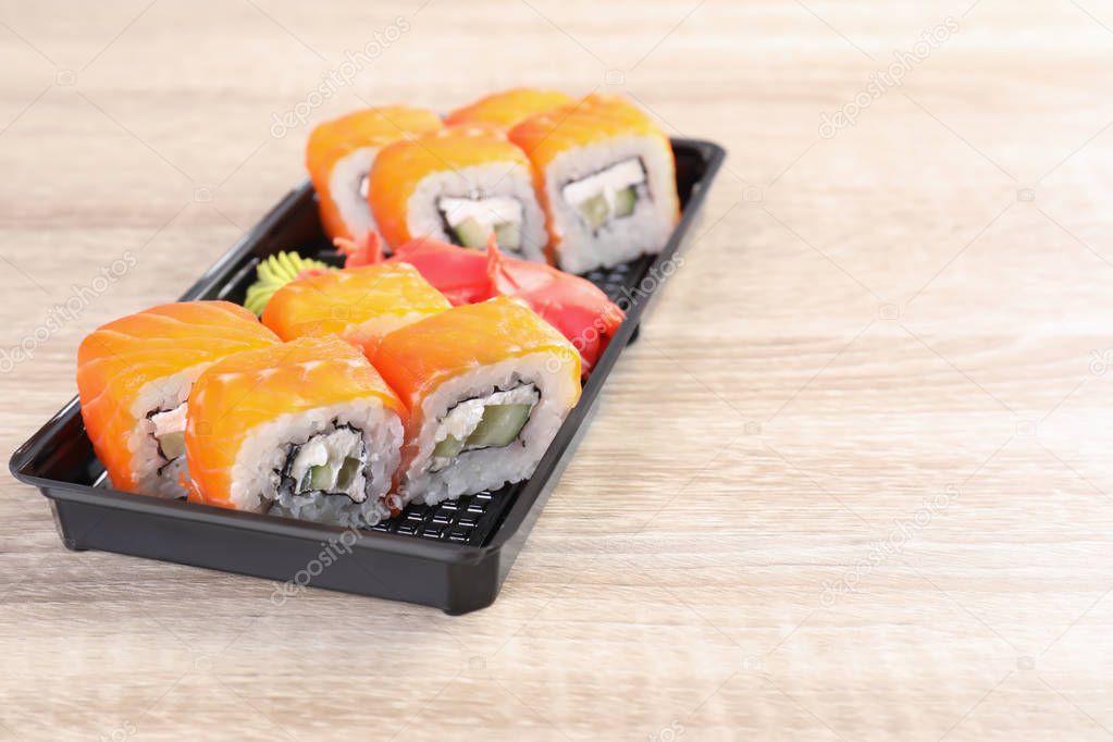 Box with tasty sushi rolls on wooden table, space for text. Food delivery