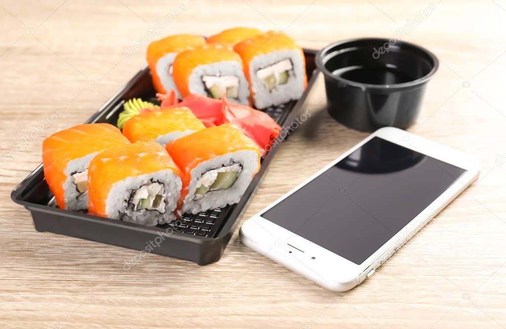 Smartphone with space for text and sushi rolls served on wooden table. Food delivery