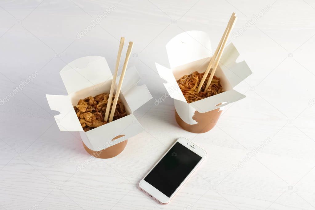 Mobile phone with space for text and Chinese noodles on white wooden table. Food delivery