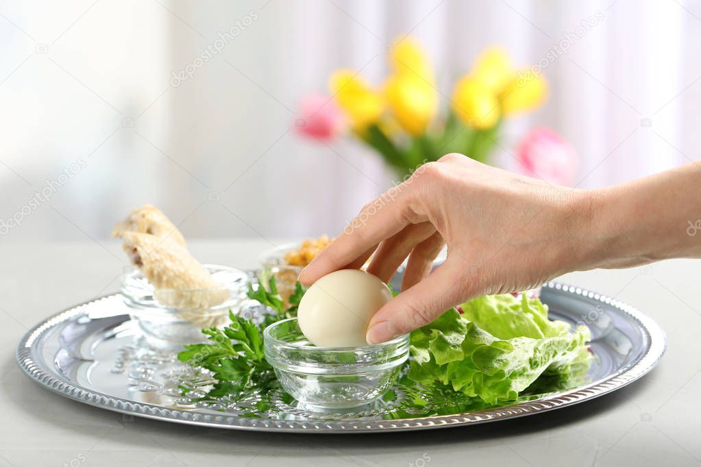 Woman holding traditional egg over Passover (Pesach) Seder plate on table, closeup. Space for text