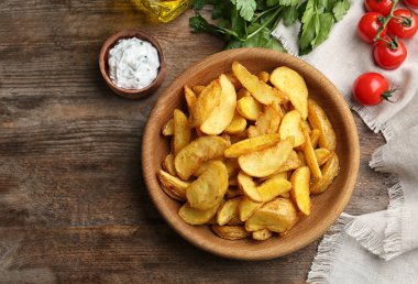 Bir kase lezzetli patates dilimleri ahşap arka plan, üstten görünüm üzerinde pişmiş. Metin için yer