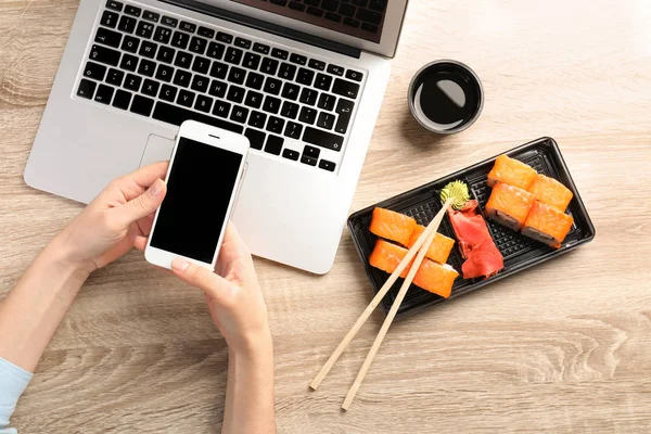 Nő, okostelefon, a laptop és a finom sushi tekercs, fából készült asztal, szöveg adható. ÉTELFUTÁR — Stock Fotó