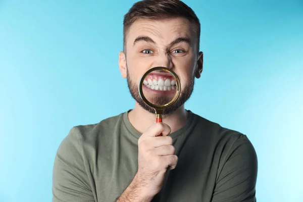 Hombre joven con dientes sanos y lupa sobre fondo de color — Foto de Stock