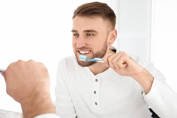 Joven limpiando dientes contra espejo en el baño — Foto de Stock