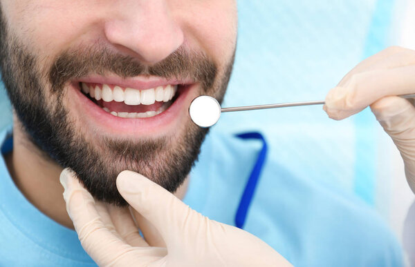 Dentist examining young man's teeth with mirror, closeup