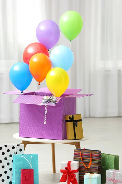 Caixa de presente com balões de ar brilhante e sacos de presente dentro de casa — Fotografia de Stock