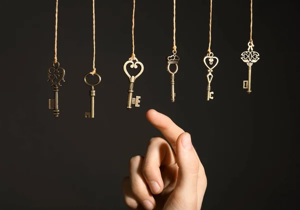 Woman choosing among bronze vintage ornate keys hanging on threads against dark background, closeup — Stock Photo, Image