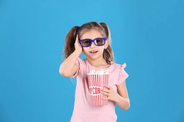 Niedliches kleines Mädchen mit Popcorn und Gläsern auf farbigem Hintergrund — Stockfoto