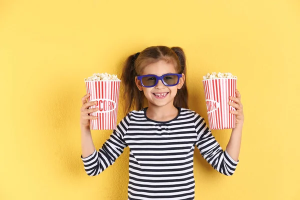 Niedliches kleines Mädchen mit Popcorn und Gläsern auf farbigem Hintergrund — Stockfoto