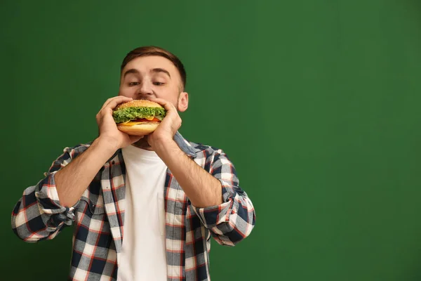 Young man eating tasty burger on color background. Space for text — Stock Photo, Image