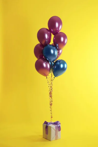 Ljusa ballonger och presentförpackning på färgbakgrund — Stockfoto