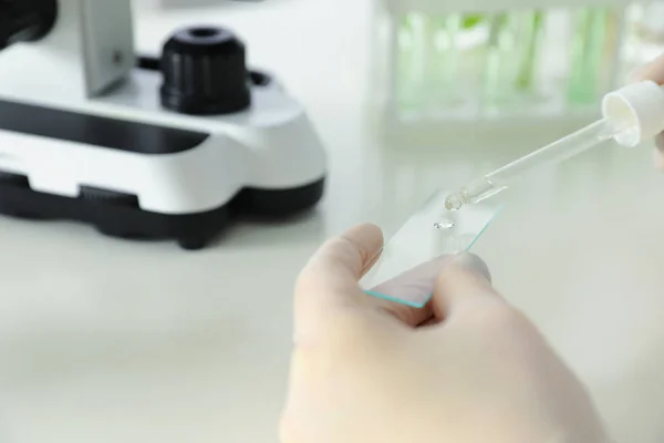 Lab assistant dropping liquid on microscope slide at table, closeup. Plant chemistry