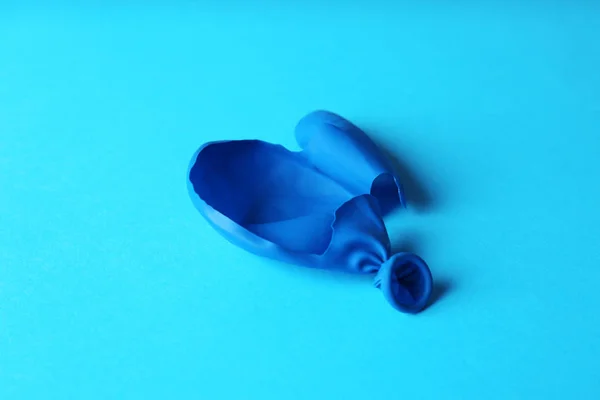 Popped blue latex balloon on color background