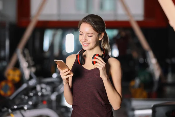 Mujer joven con auriculares y dispositivo móvil en el gimnasio — Foto de Stock