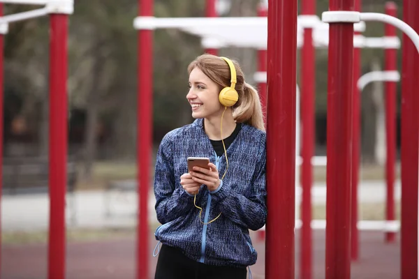 Young woman with headphones listening to music on sports ground