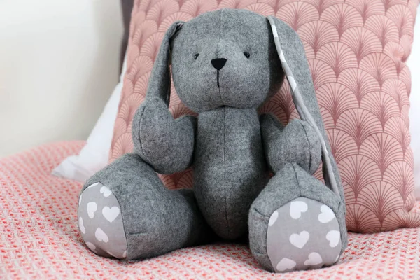 Lindo juguete conejo sentado en la cama en el interior —  Fotos de Stock